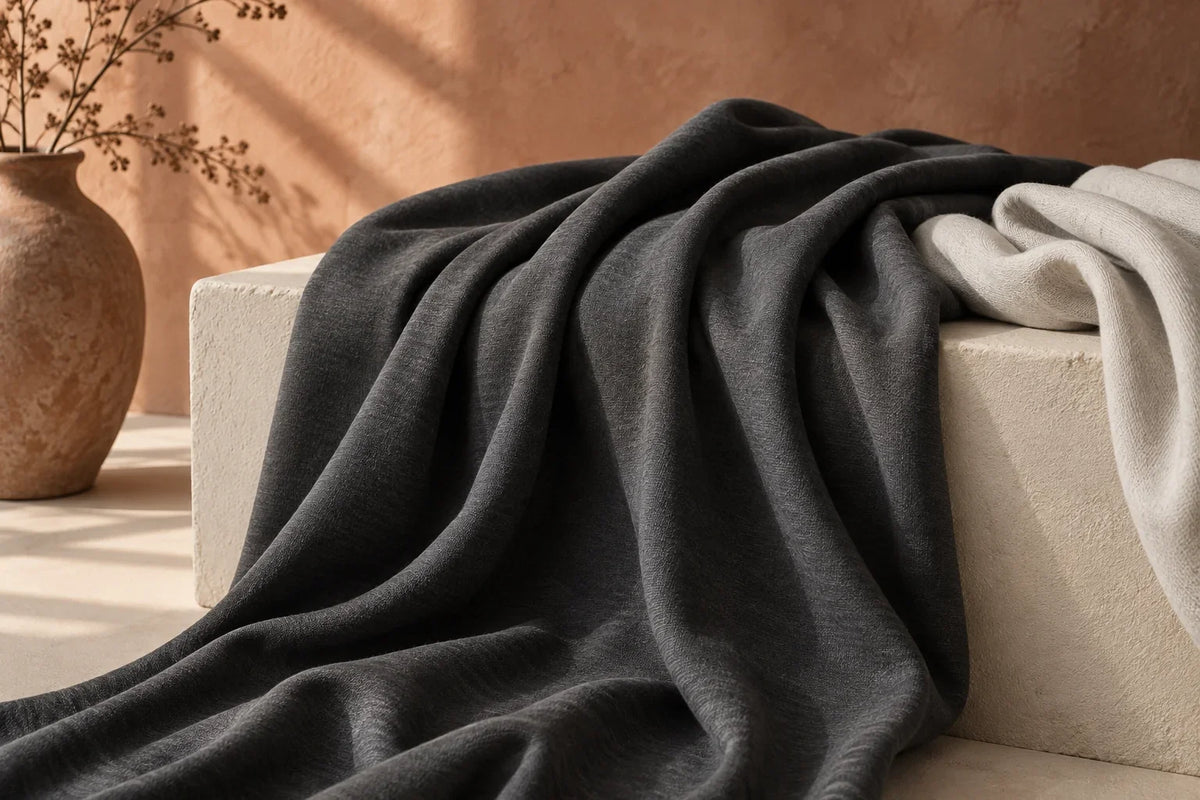 Charcoal and pearl jersey fabric draped over an ivory plinth against a warm terracotta backdrop.